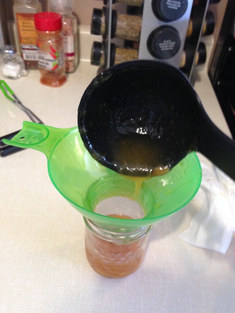 Pouring peach jam into the jar through a funnel